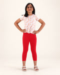 Front view of girls’ red capri leggings, styled with a floral top and sandals.