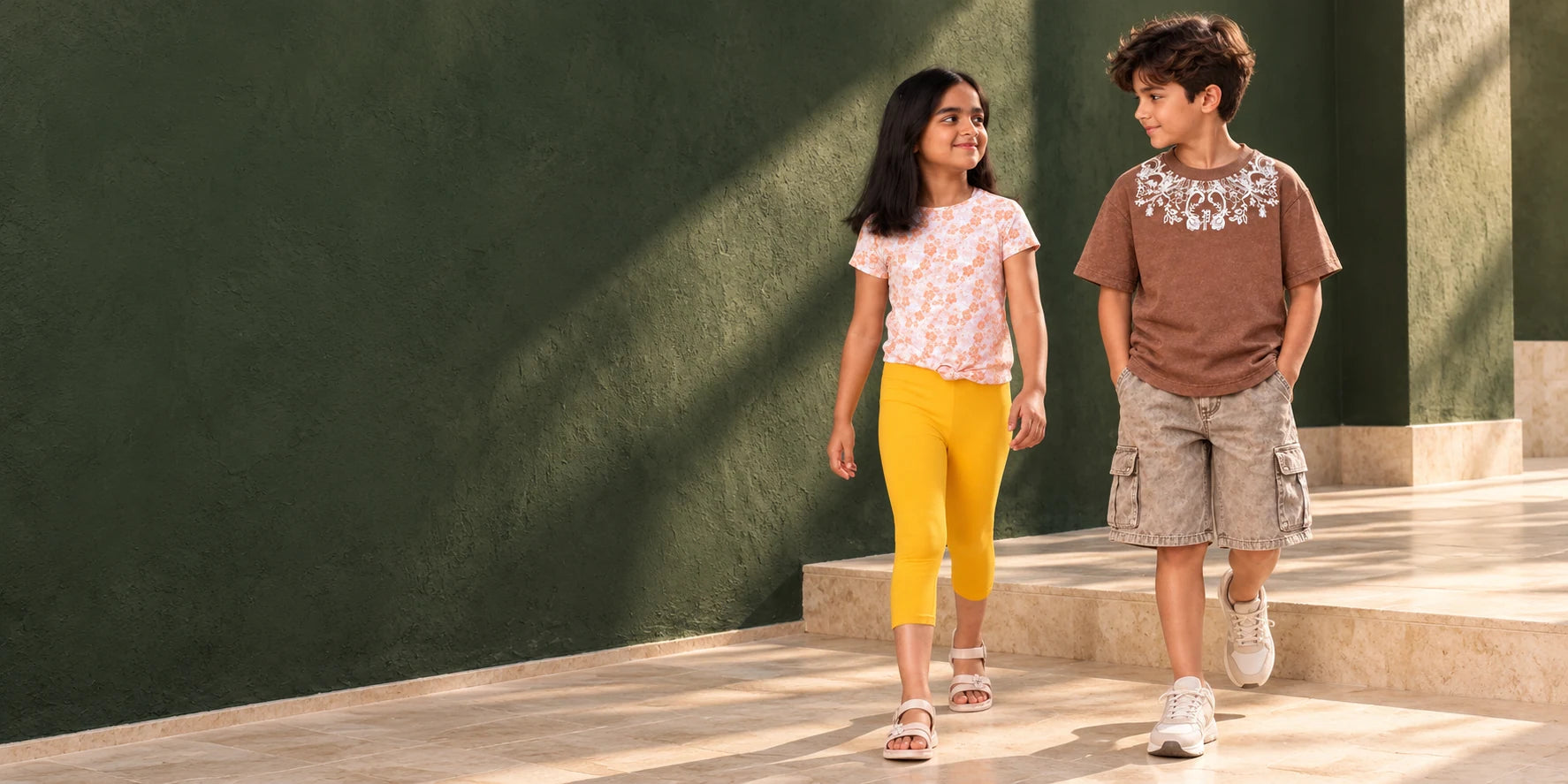 Children in a sunlit courtyard wearing a brown ornamental T-shirt and yellow capri leggings.